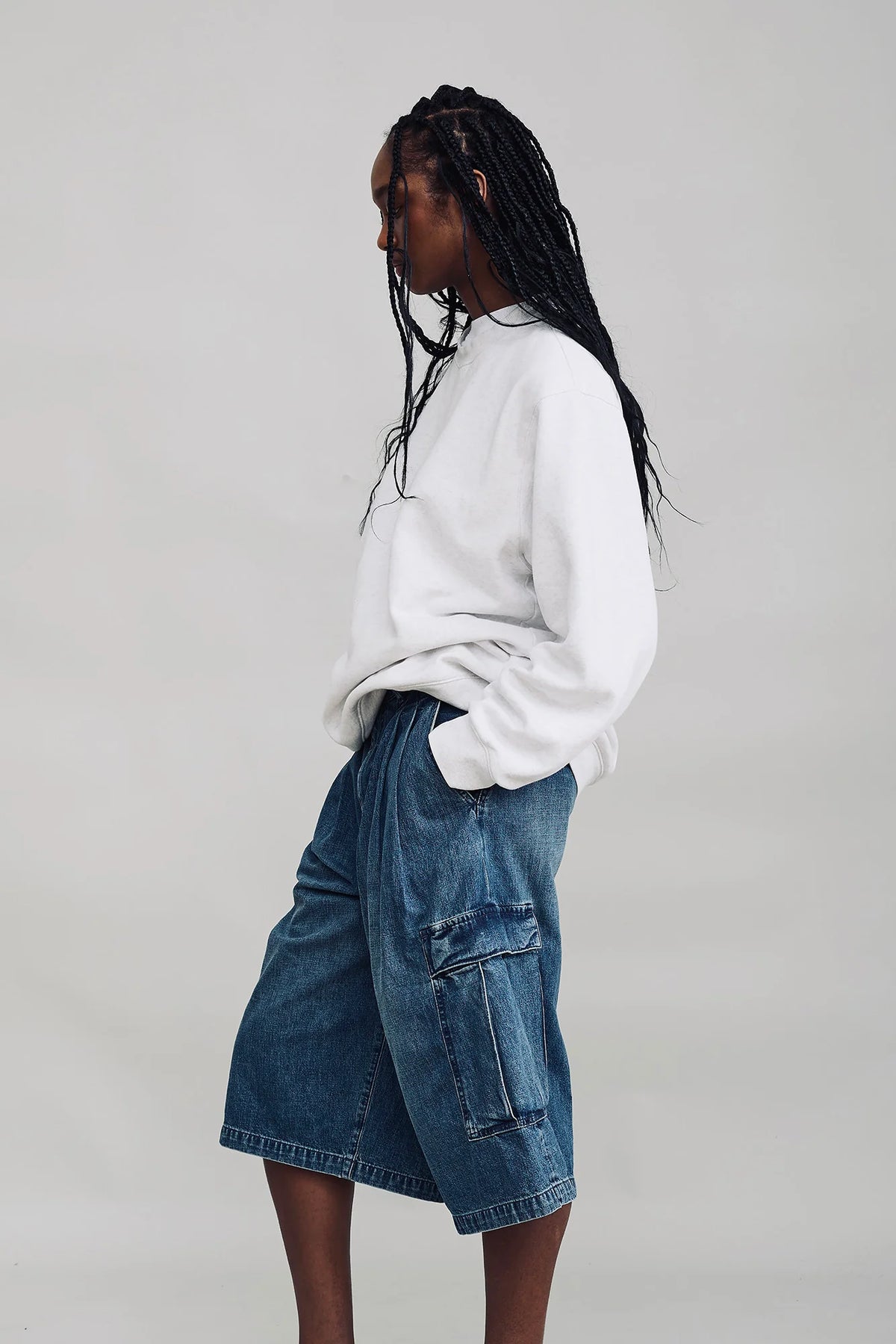 Denimist Ainsley Triple Pleat Cargo Short in white, styled with a white top, model posed sideways against gray background.
