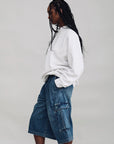 Denimist Ainsley Triple Pleat Cargo Short in white, styled with a white top, model posed sideways against gray background.