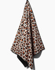 The Faire Leopard Yoga Towel features a bold orange, black, and beige leopard print and ultra-absorbent fabric, shown hanging from a hook against a white background.