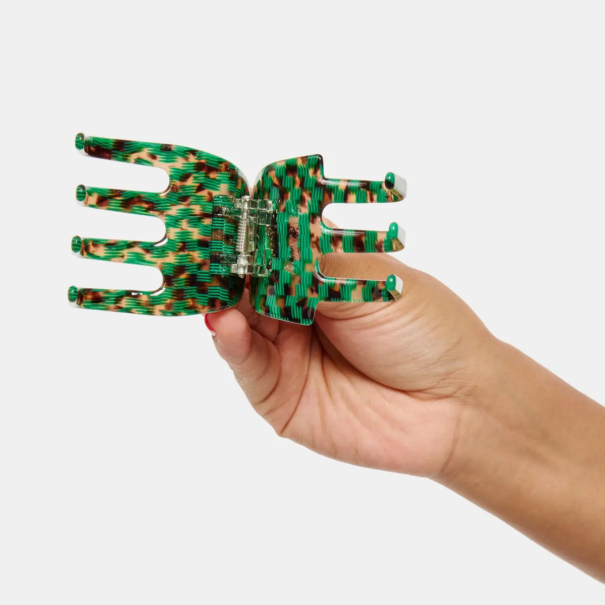 A hand holds the Faire Ursa Claw in Andi, a green and orange patterned acetate hair accessory, against a plain white background.