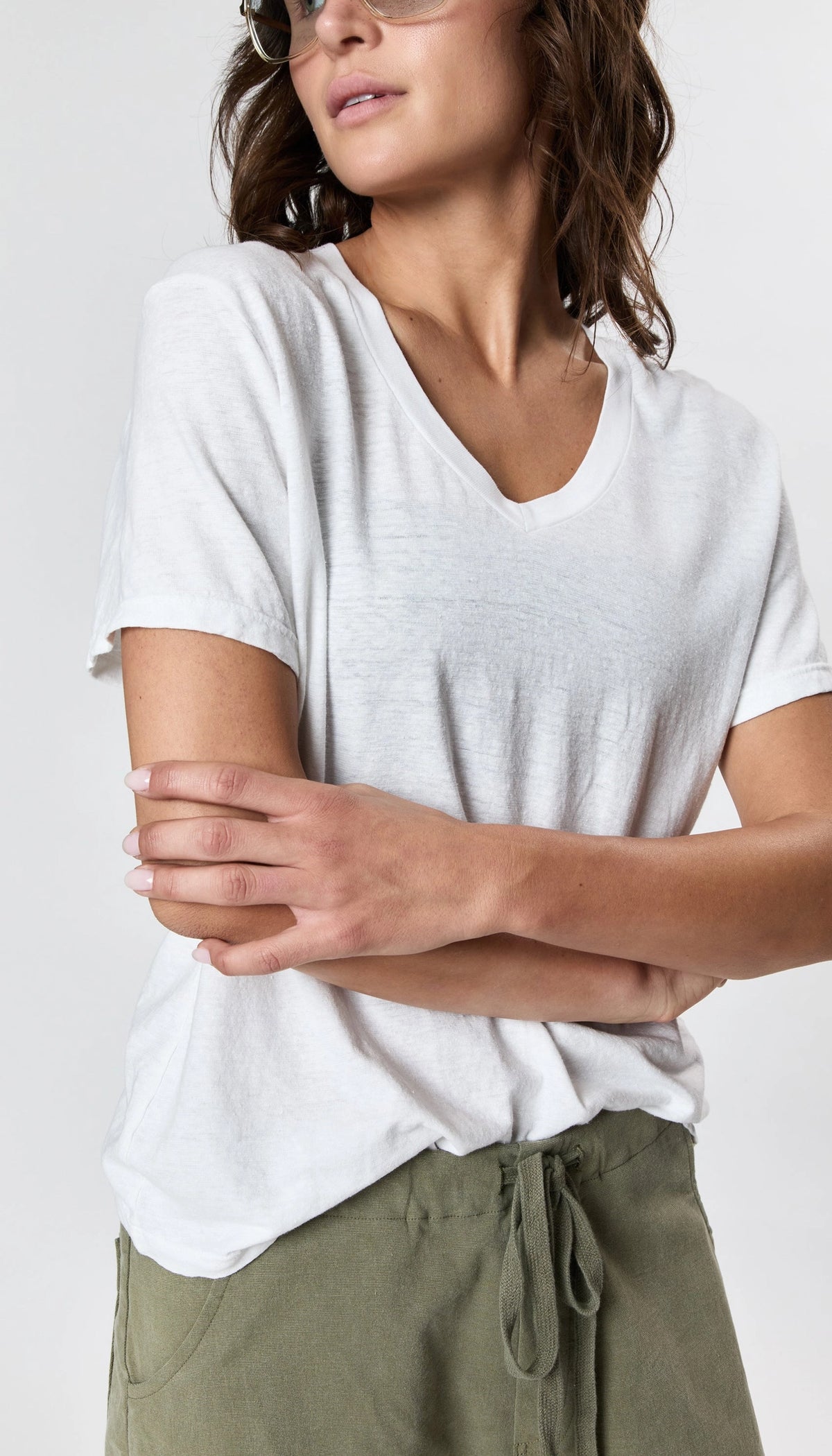 A person in the Faire Hemp V Neck t-shirt and olive green drawstring pants stands with arms crossed, facing slightly to the side against a plain white background. Their face is partially visible.