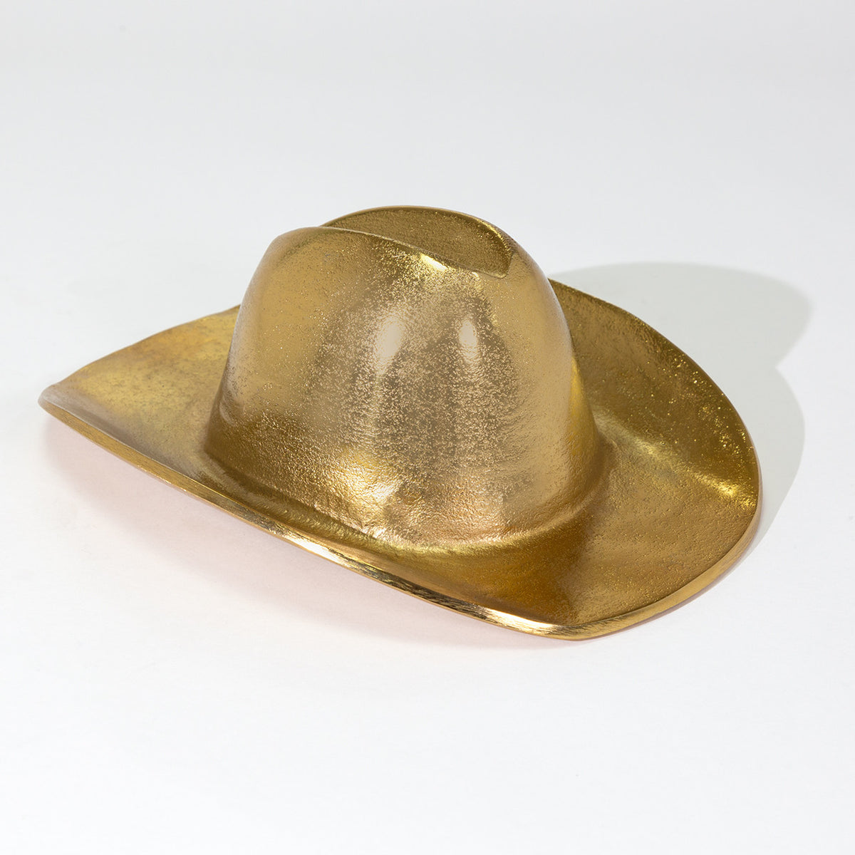 The Import Collection's Westin Hat is a shiny, metallic gold cowboy hat sculpture on a white surface, casting a soft right shadow—a bold gold accent ideal for western home decor.