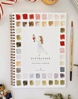 The Faire Watercolor Workbook, a spiral-bound beginner’s guide titled "Nutcracker," features a ballerina cover and paint swatches. Shown with a brush, nutcracker ornament, ribbon, and greenery for a festive touch.