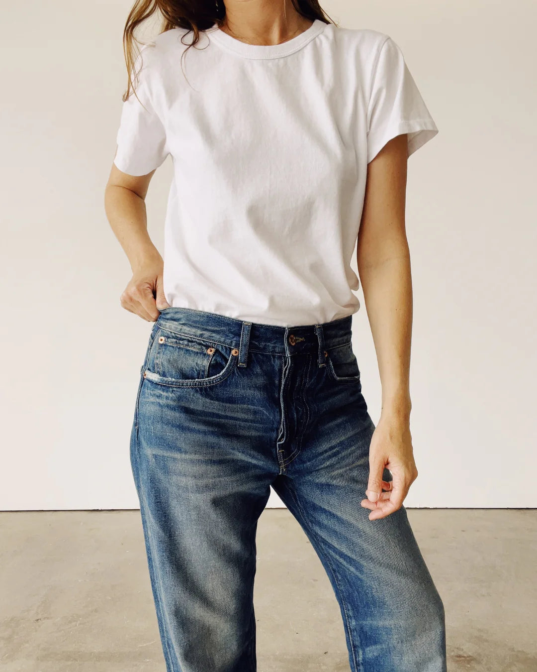 A person wearing "The Crew" plain white 100% cotton T-shirt by Hey Gang and blue jeans stands against a neutral backdrop, one hand casually in the pocket. The relaxed pose highlights the enzyme-washed style of this vintage find.