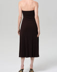 A person is seen from behind wearing the Citizens Of Humanity/AGOLDE mila halter dress in chocolate brown with heeled sandals, standing against a plain light gray background.