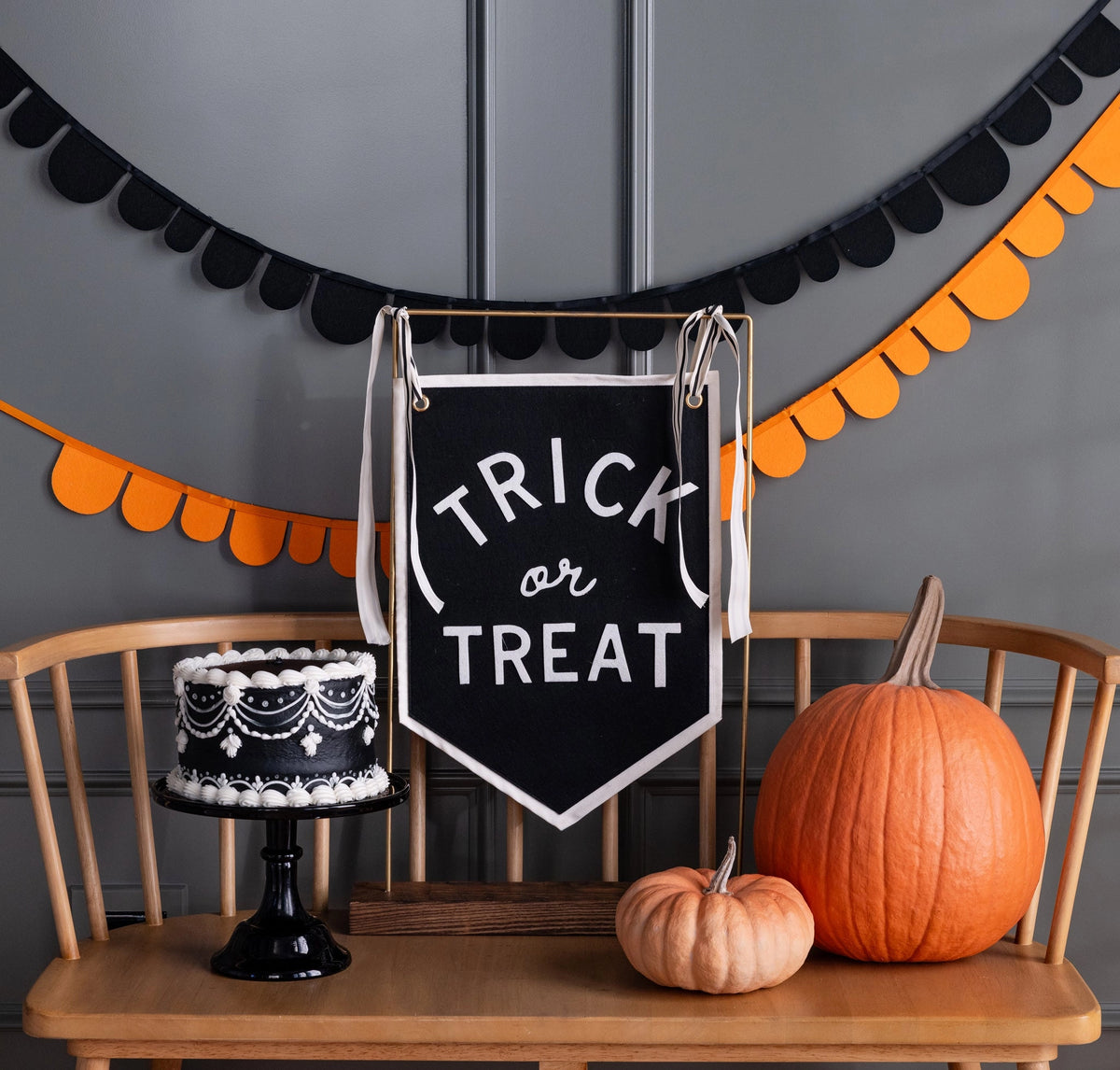 Pumpkins and a black cake on a bench with festive Halloween decor and Faire Trick or Treat banner, Bungalow Furniture.