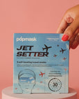 A hand with pink nail polish holds a box of "Faire Eye Masks" against a pink background. The packaging showcases sky and plane graphics, promoting the unisex steam masks as ideal for a relaxing journey within 30 seconds.