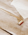 The Faire Candle Snuffer, a sophisticated candle accessory, rests on a beige linen surface beside a white cloth.