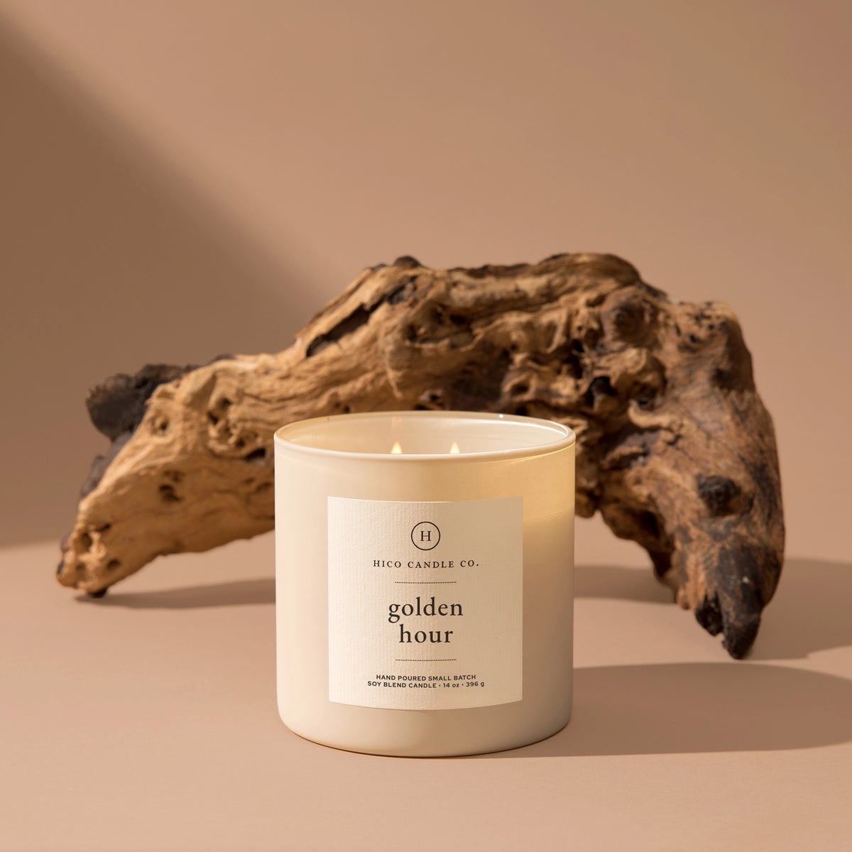 The Faire Golden Hour - 14oz. Candle features a passion fruit scent and soy wax, displayed in a glass jar on a beige surface with driftwood and soft lighting for a neutral, inviting ambiance.