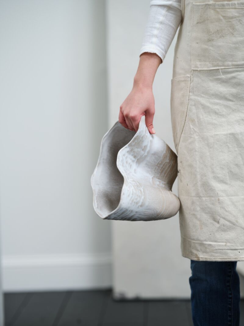 Claribel Vase Tall by Accent Decor, sculptural wavy ceramic, held by person in beige apron indoors.