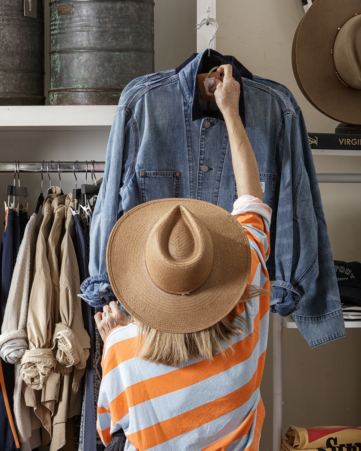 Denim jacket displayed in a chic boutique as a stylish shopper in stripes and a hat browses the clothing rack.