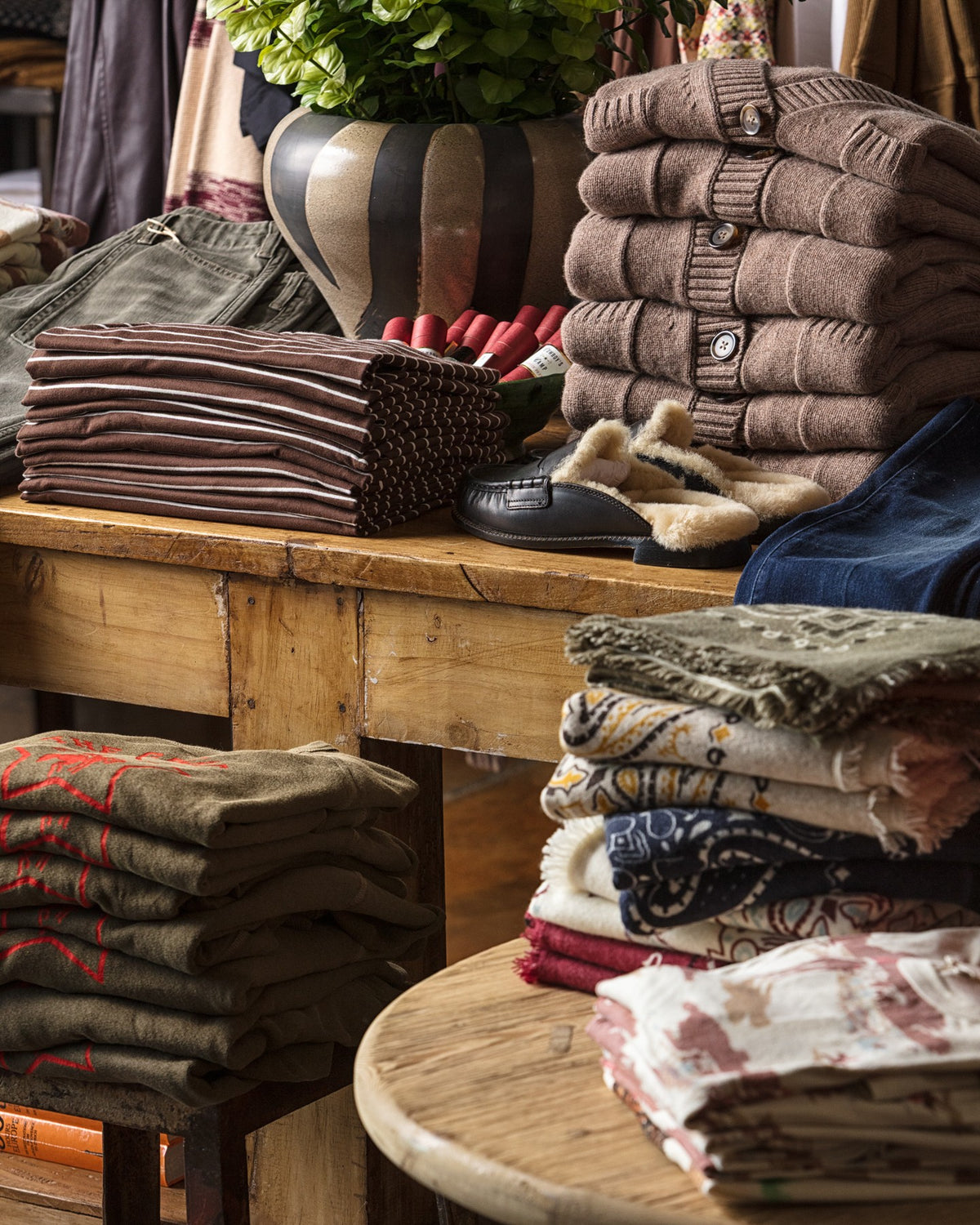Cozy folded knits and accessories arranged on wooden tables, styled in a welcoming Bungalow showroom setting.