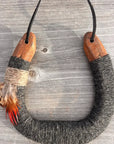 The Faire Lucky Horseshoe features an upcycled horseshoe wrapped in gray wool with wooden ends, twine, and feathers, hanging by a black cord—making it a unique housewarming gift.