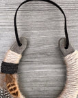 The Lucky Horseshoe by Faire, wrapped in beige and gray twine with left-side feathers and a black cord, sits on weathered wood—perfect as a personalized or unique housewarming gift.