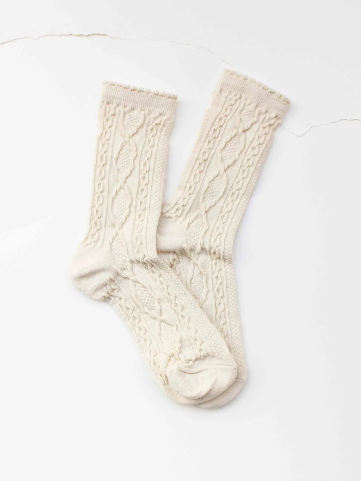 Faire Twist Cotton Crew Socks in cream feature a textured cable knit pattern and are shown overlapping on a white surface.