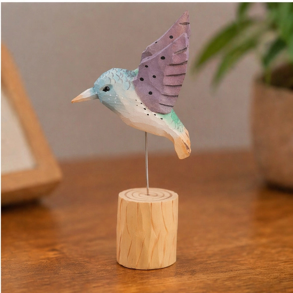Purple hand-painted carved hummingbird by Faire on a wooden stand, displayed on a brown table.