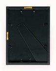 A black Faire frame, shown from the back with metal clips, a stand, and hanging hardware, is ready to display Cezanne’s "The Peppermint Bottle"—ideal for showcasing limited-edition art against a plain white background.