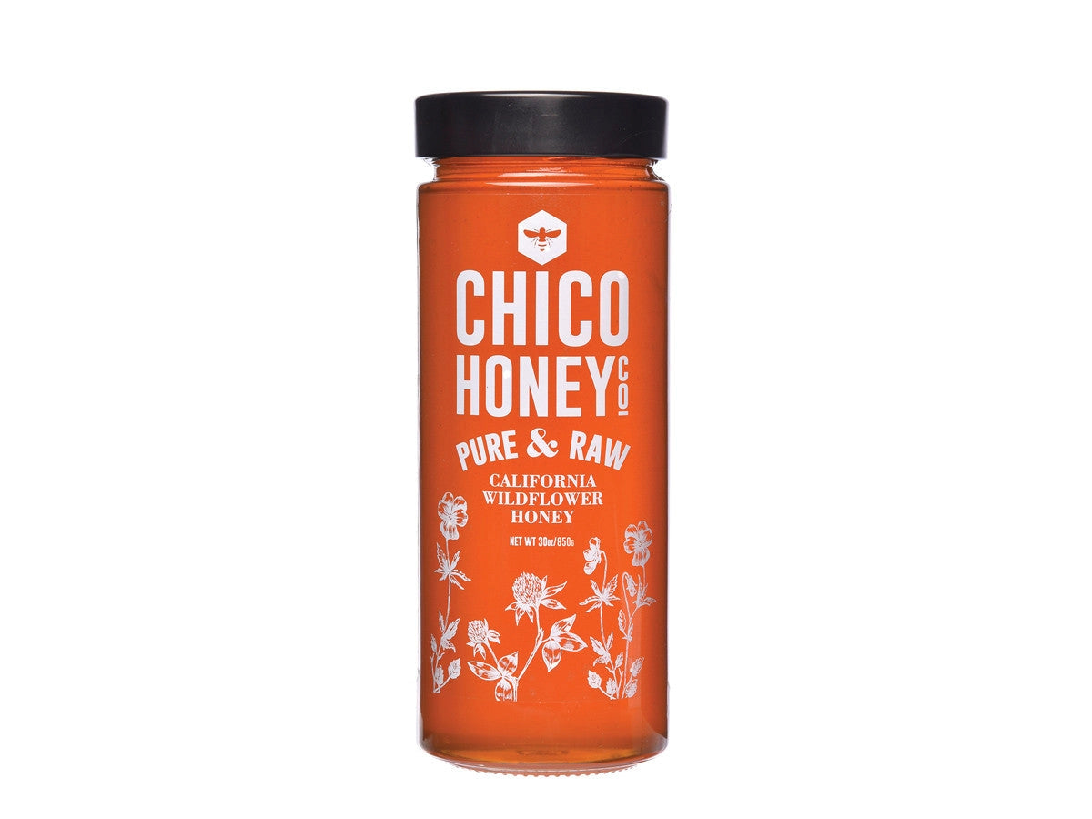 A tall glass jar with a black lid, filled with golden honey. The label reads "Olivarez Chico Honey" by Faire and features white floral illustrations at the bottom.