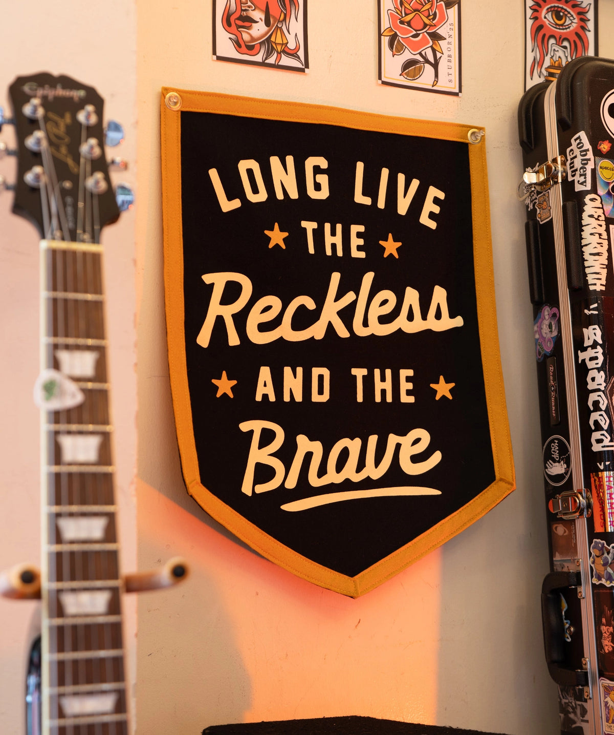 Black and gold camp flag by The Faire displayed beside a stickered guitar case for a creative home decor touch.