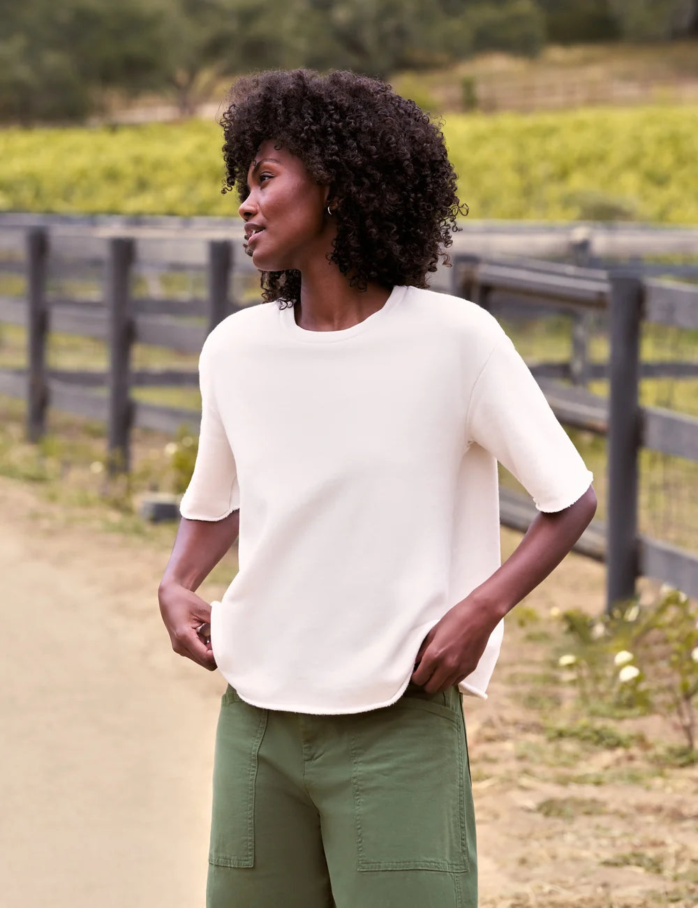 Green pants styled with a Frank & Eileen Perry NYC Crew Tee, worn casually outdoors by a wooden fence.