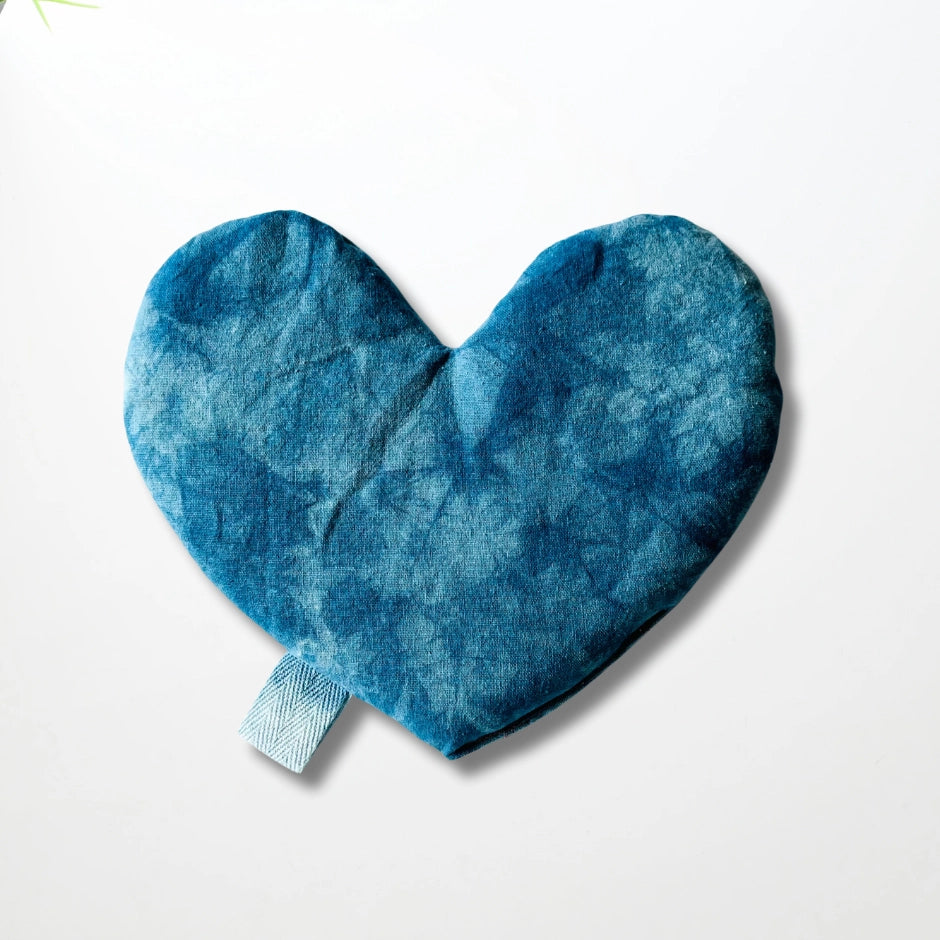 The Faire Heart Eye Pillow is a soft, blue, heart-shaped cotton pillow with a side loop tag, shown on a plain white background—ideal for soothing anxiety relief.