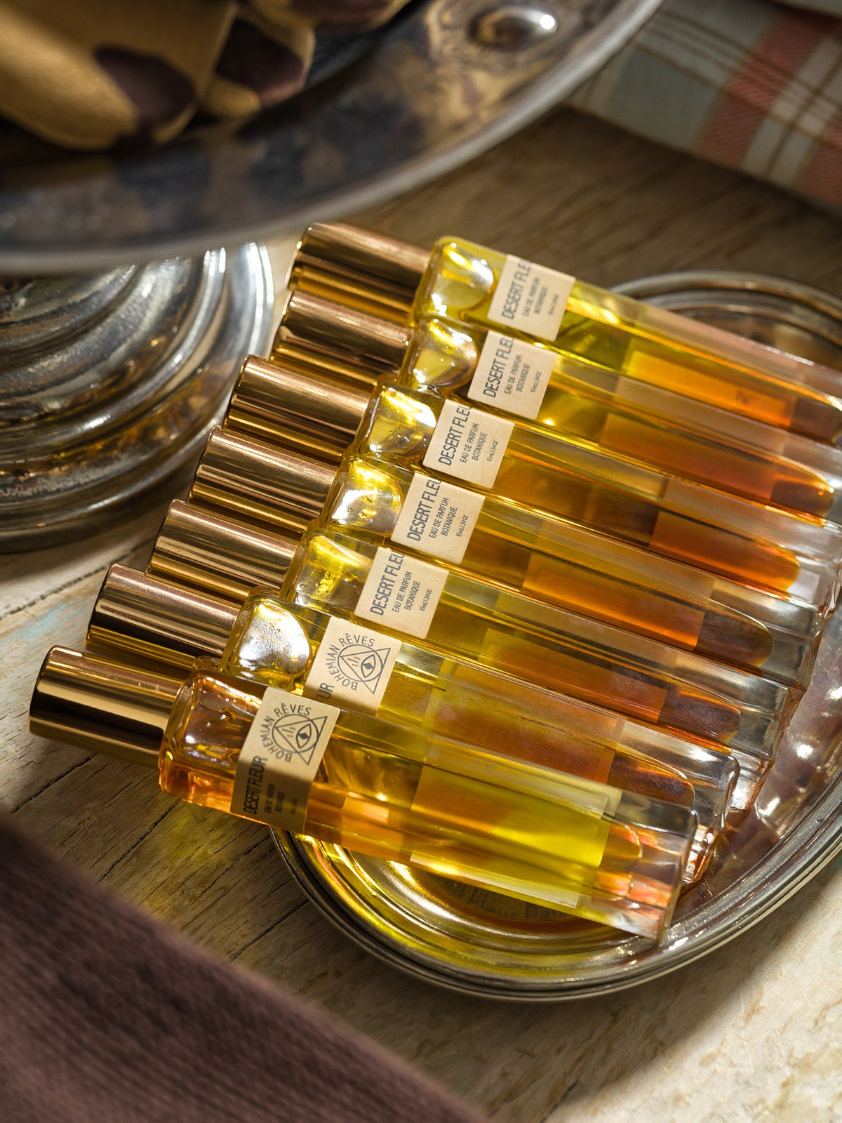 Elegant glass perfume bottles with gold caps on a silver tray, glowing in warm sunlight for Bungalow Furniture & Accessories.