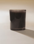 Dark brown oud-scented candle in clear glass by Bungalow, Faire Bougie D’oud, on a white surface.