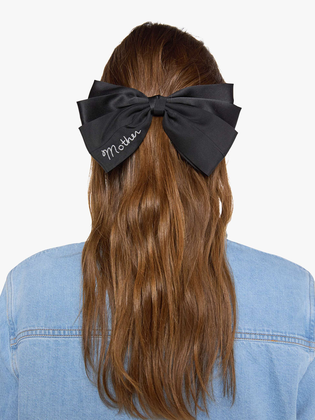 Black silk hair bow with cursive white text clipped in brown hair by Bungalow Furniture &amp; Accessories.
