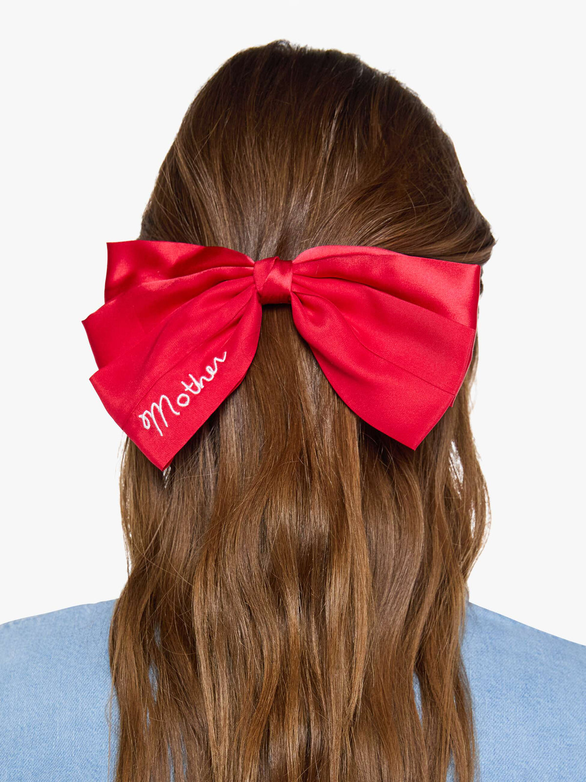 Red satin hair bow with white embroidered text from Bungalow Furniture &amp; Accessories worn in brown hair.