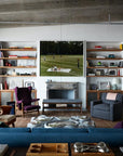 A stylish living room showcases eclectic furniture, a blue sofa, and art, as seen in "Robert Stilin New Work" by Hachette Book Group. Expansive windows fill the space with light and bookshelves display striking artwork above the fireplace.