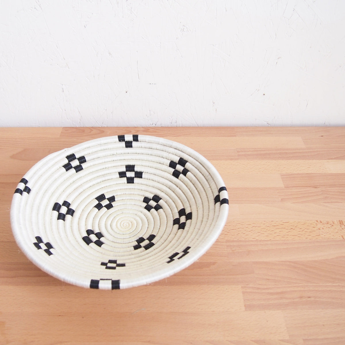 Small black sisal Maraba bowl by Faire with geometric weaving, shown on light wood against a white wall.