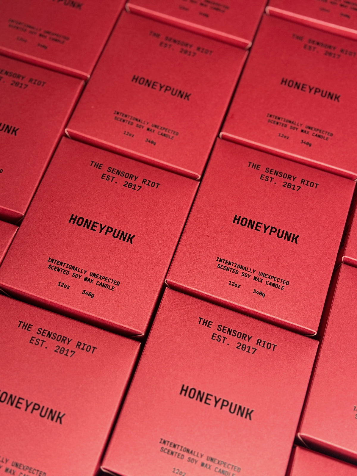Several HONEYPUNK 12 oz candles by Faire are arranged in a grid, each box labeled with "The Sensory Riot Est. 2017" and "Intentionally Unexpected Spiced Honey Scented Soy Wax Candle.