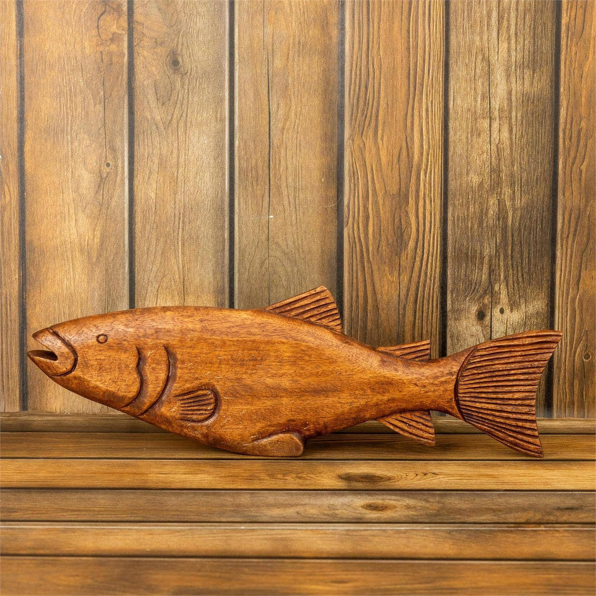 The Faire Rustic Carved Wood Fish Figure features intricate details and is displayed against a wooden plank wall, making it an ideal accent for rustic lake house or coastal cabin decor.