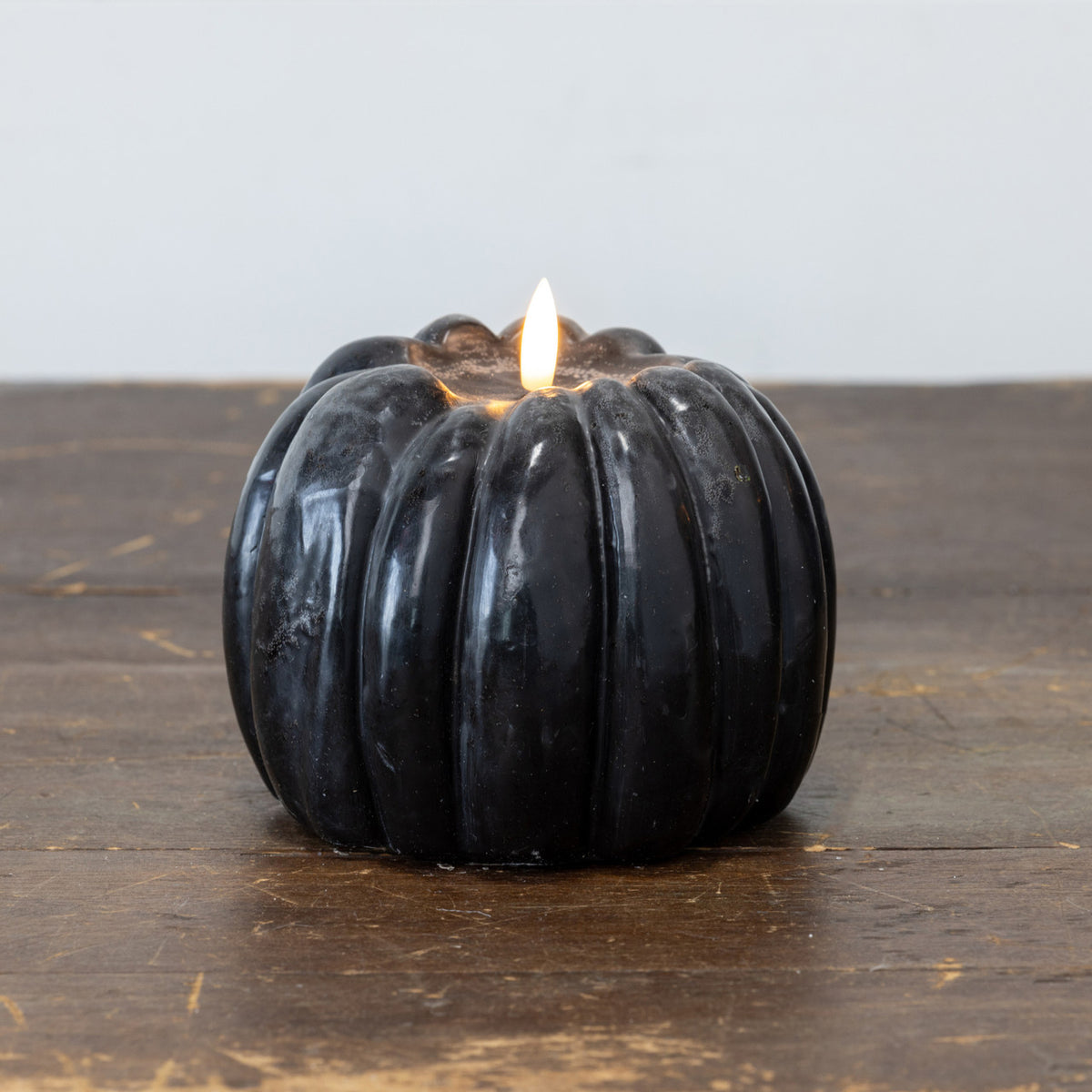 Black pumpkin candle with 3D flame and 6-hour timer by Faire, shown on a wooden surface.