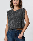 A woman with wavy brown hair wears the Faire Hemp Jackie Pleat Shell Bandana top and blue jeans, standing against a plain light gray background. She looks at the camera with a relaxed expression and one hand by her side.
