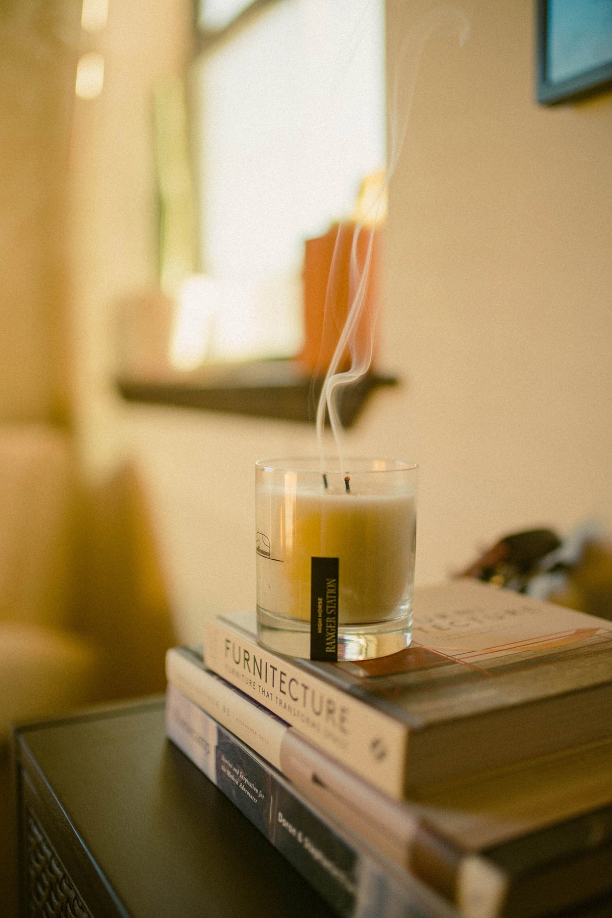 High Horse candle in a glass jar, lit with wisps of smoke, resting on a stack of books.