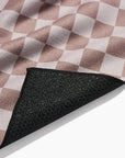 The Faire Chic Checker Yoga Towel features a soft pink and white checkerboard fabric and a black, slip-resistant rubberized underside, shown partially folded.