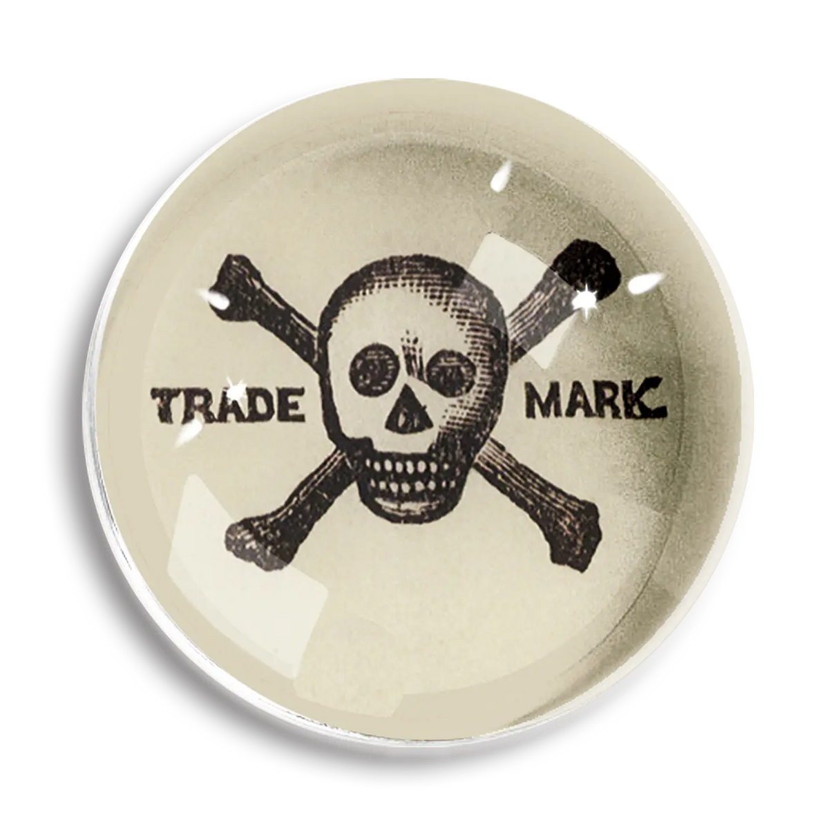 The Ben's Garden Dome Crystal Paperweight features a black skull and crossbones on an off-white background, with "TRADE" and "MARK" flanking it. Inspired by New York studio style, it evokes the charm of handcrafted French crystal.