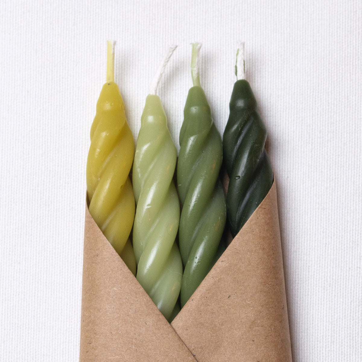 The Woodland Spiral Beeswax Candles S/4 by Faire features four handcrafted candles in yellow and green shades, wrapped in brown paper—thoughtfully made in the Catskills, NY.