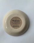 An upside-down Ring Bowl by Faire is shown, revealing its textured base and a brown label: "Rosemary for remembrance, friendship & love. csfceramics.com"—a jewelry catchall inspired by botanical symbolism.