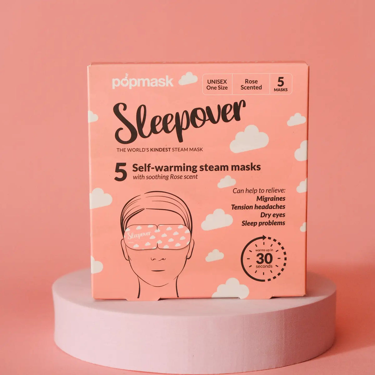 A pink box of "Faire eye masks" contains 5 rose-scented self-warming steam masks for migraines, tension headaches, and dry eyes relief. Positioned on a circular platform with a pink background, they're perfect for your next jet setter adventure!.