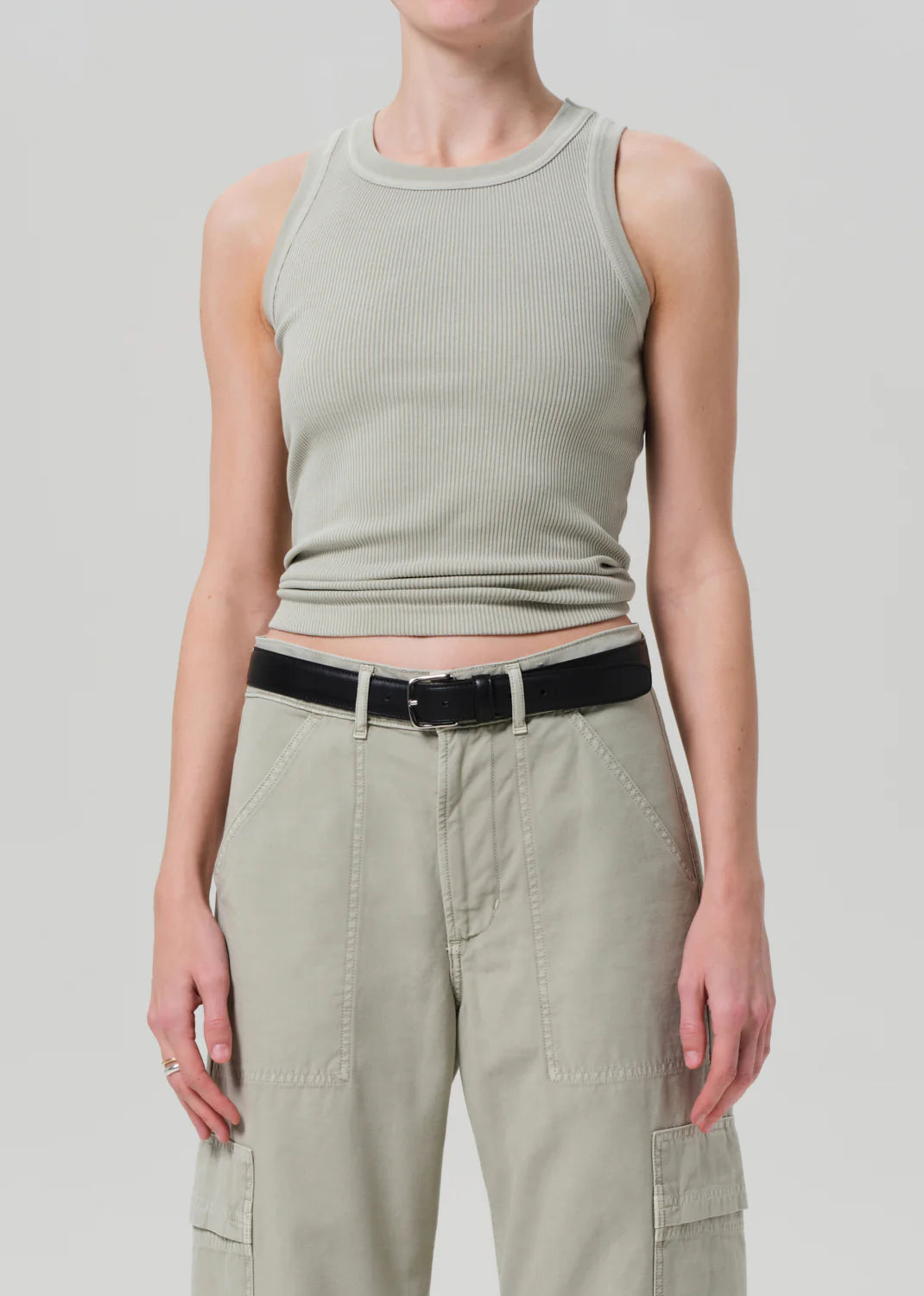 A person wears a light gray Isabel Rib Tank by Citizens Of Humanity/AGOLDE with high-waisted, light olive green pants and a black belt. Their arms are relaxed by their sides against a plain gray background. This versatile tank is perfect for layering with any outfit.