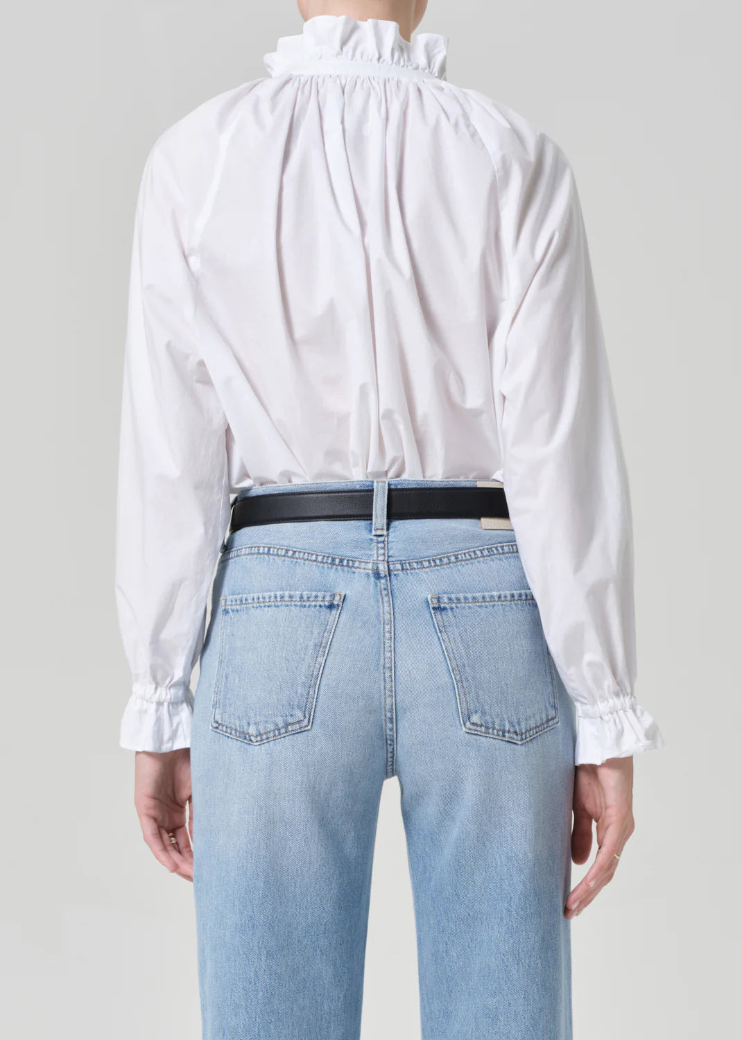 A person is shown from the back against a plain light gray background wearing Citizens Of Humanity/AGOLDE's loretta ruffle top in optic white and light blue high-waisted jeans.