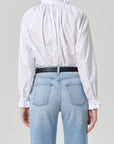 A person is shown from the back against a plain light gray background wearing Citizens Of Humanity/AGOLDE's loretta ruffle top in optic white and light blue high-waisted jeans.