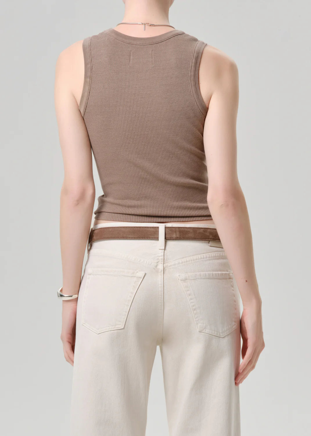 A person is seen from behind wearing the Citizens Of Humanity/AGOLDE nova tank, featuring a scoop neckline, paired with high-waisted off-white jeans. Their arms rest naturally at their sides against a plain light gray backdrop.
