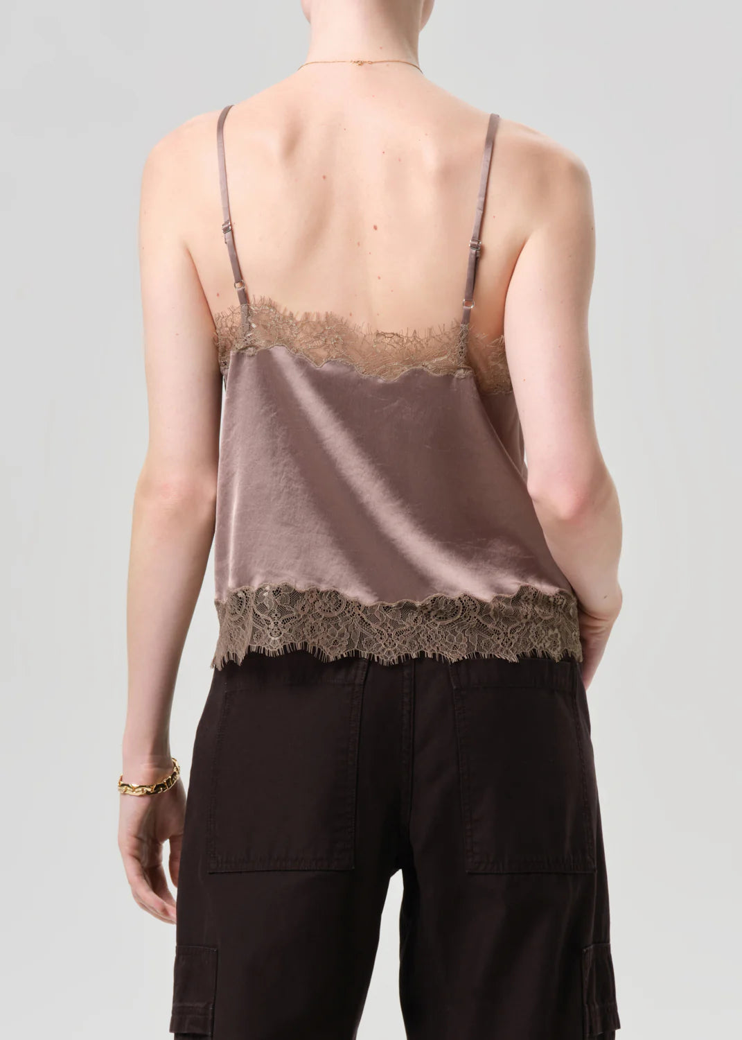 A person is shown from the back against a light grey background, wearing the Citizens Of Humanity/AGOLDE lace trimmed cami made from Japanese hammered satin with lace accents on top and bottom edges, paired with dark pants.
