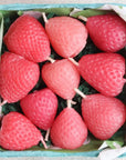 A box of twelve Faire Pink Strawberry Birthday Candles, shaped like strawberries with white wicks and arranged on green paper shreds. These eco-friendly candles add a charming touch to any celebration.