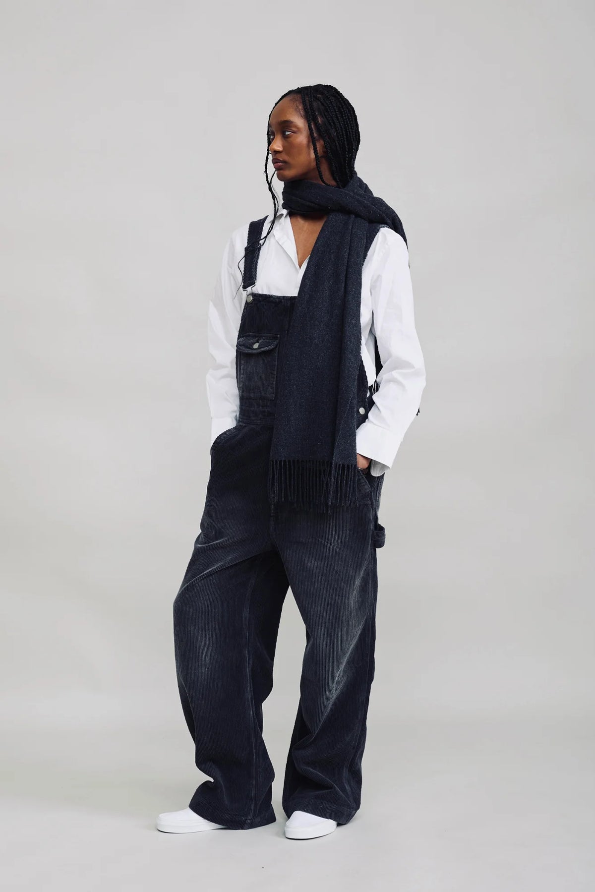 Black corduroy wide-leg SLOUCH BIB OVERALL by Denimist worn over a white shirt with a matching scarf.