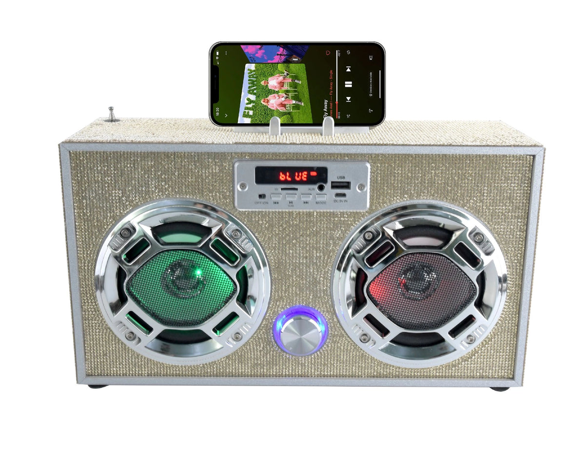 The Faire Gold Bling Wireless Boombox with FM Radio features two round LED speakers—one glowing green, the other red—a digital display, control buttons, and a docked smartphone on top playing music in retro vintage style.