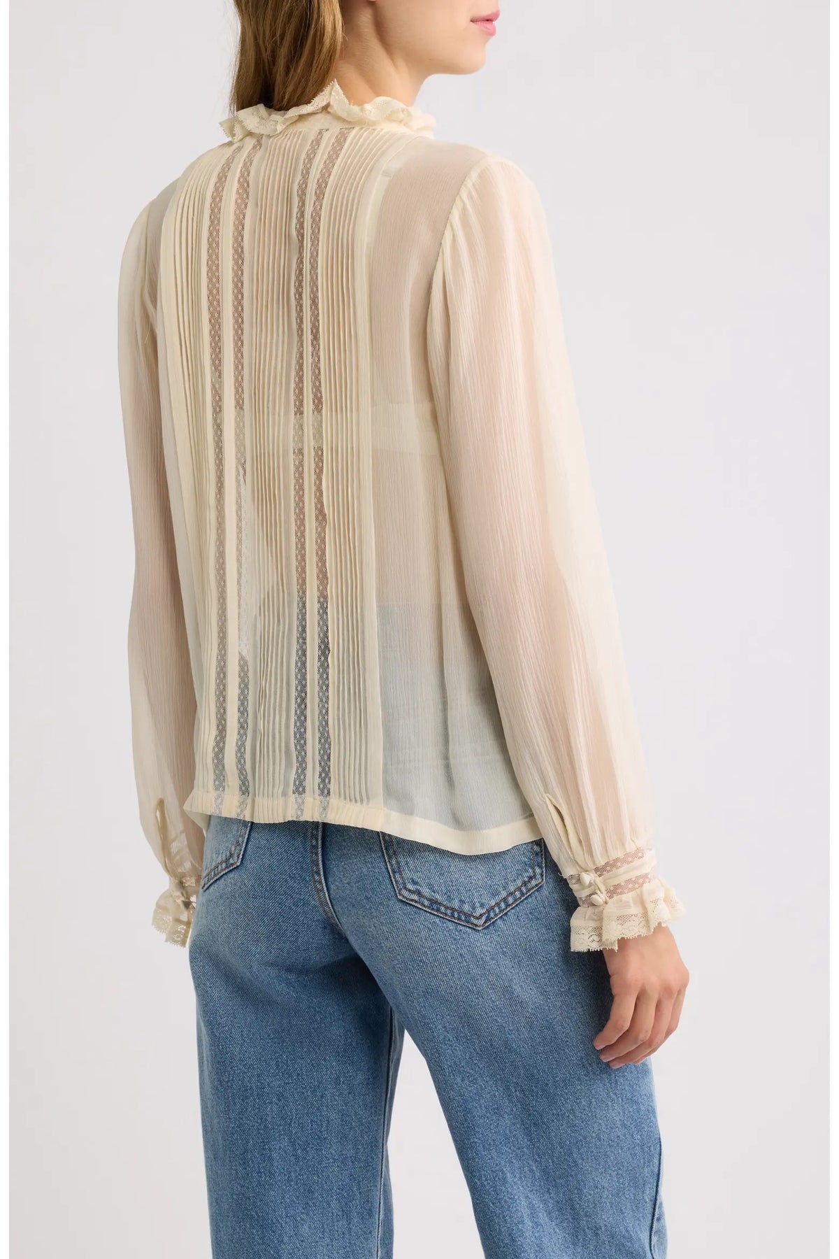 Sheer cream Magdeleine Top with lace ruffles by DOEN, styled casually with blue jeans, back view.